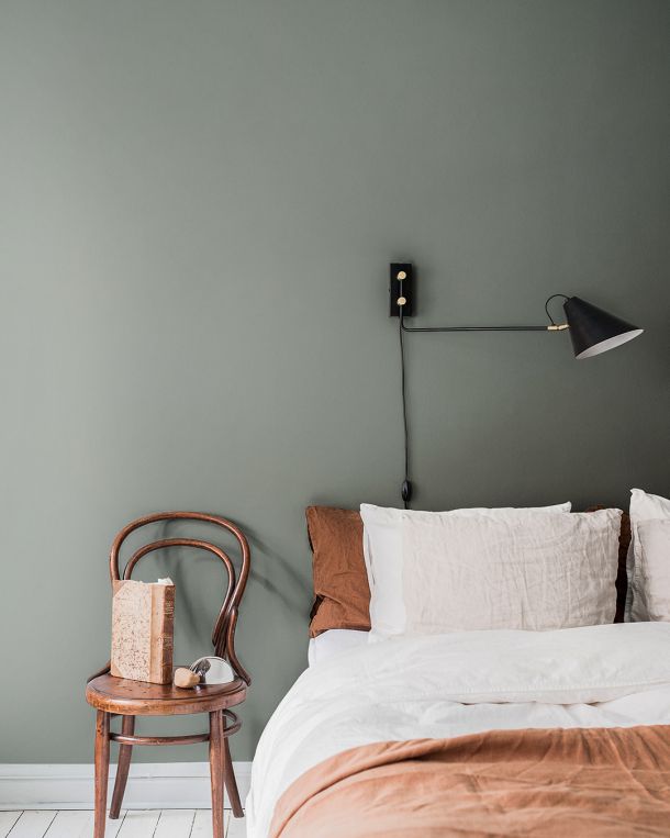 Grågrön enfärgad tapet i ett sovrum men en bäddad säng med orange sängkläder